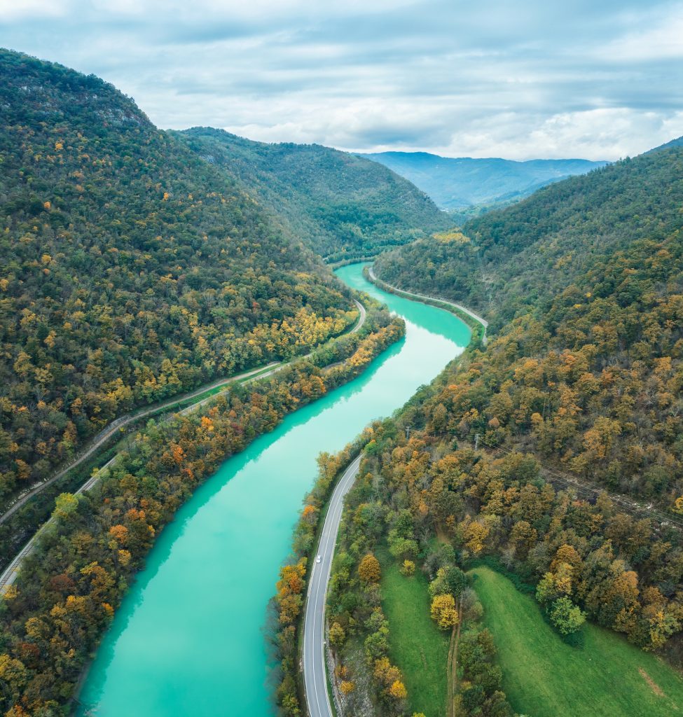 Scenic view of the emerald-green Soča River, surrounded by lush forests and mountain peaks.